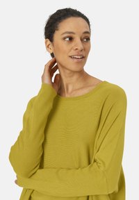 Pull à manches longues, surdimensionné, en tricot côtelé vert olive. Encolure large et coupe décontractée. Texture douce avec des détails de drapé subtils.