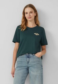 T-shirt en coton vert foncé avec un col rond et des manches courtes, présentant un design de texte "GOOD TIMES ONLY" de couleur claire sur la poitrine.