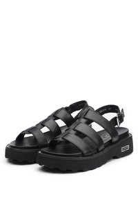 Sandali in pelle nera con fascette incrociate, fibbia regolabile alla caviglia, suola spessa e texturizzata, e design con piattaforma. Stile durevole e aperto davanti.