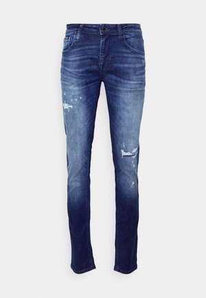 Jean bleu slim pour homme avec lavage délavé et détails usés sur les cuisses et les genoux, vue de face sur fond uni.