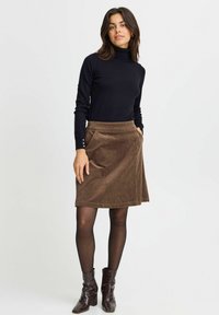 Jupe en velours côtelé marron en forme A avec poches latérales, associée à un col roulé noir et des bottines noires texturées. Tissu lisse avec des lignes verticales.