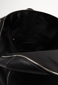 Svart läderryggsäckens inre med en slät textur, ett dragkedjefack längs baksidan och ett överdraget dragkedjestängning.