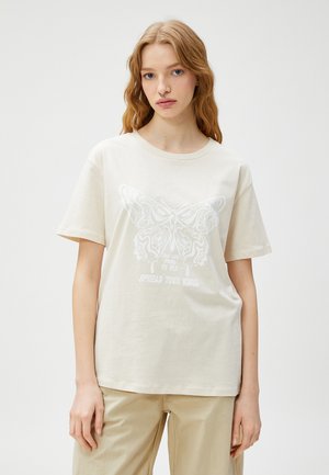 Cremefarvet bomulds T-shirt med et hvidt sommerfuglegrafik og tekst, med en afslappet pasform og korte ærmer. Glat tekstur, enkelt design.