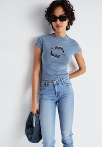 T-shirt ajusté bleu clair à manches courtes avec un motif imprimé de deux dauphins. Assorti à un jean en denim clair taille haute.