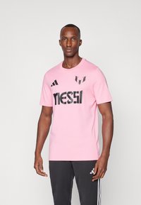 Pink t-shirt made of cotton with short sleeves, featuring black "MESSI" logo and accents from Adidas. Simple round neckline and casual fit.
