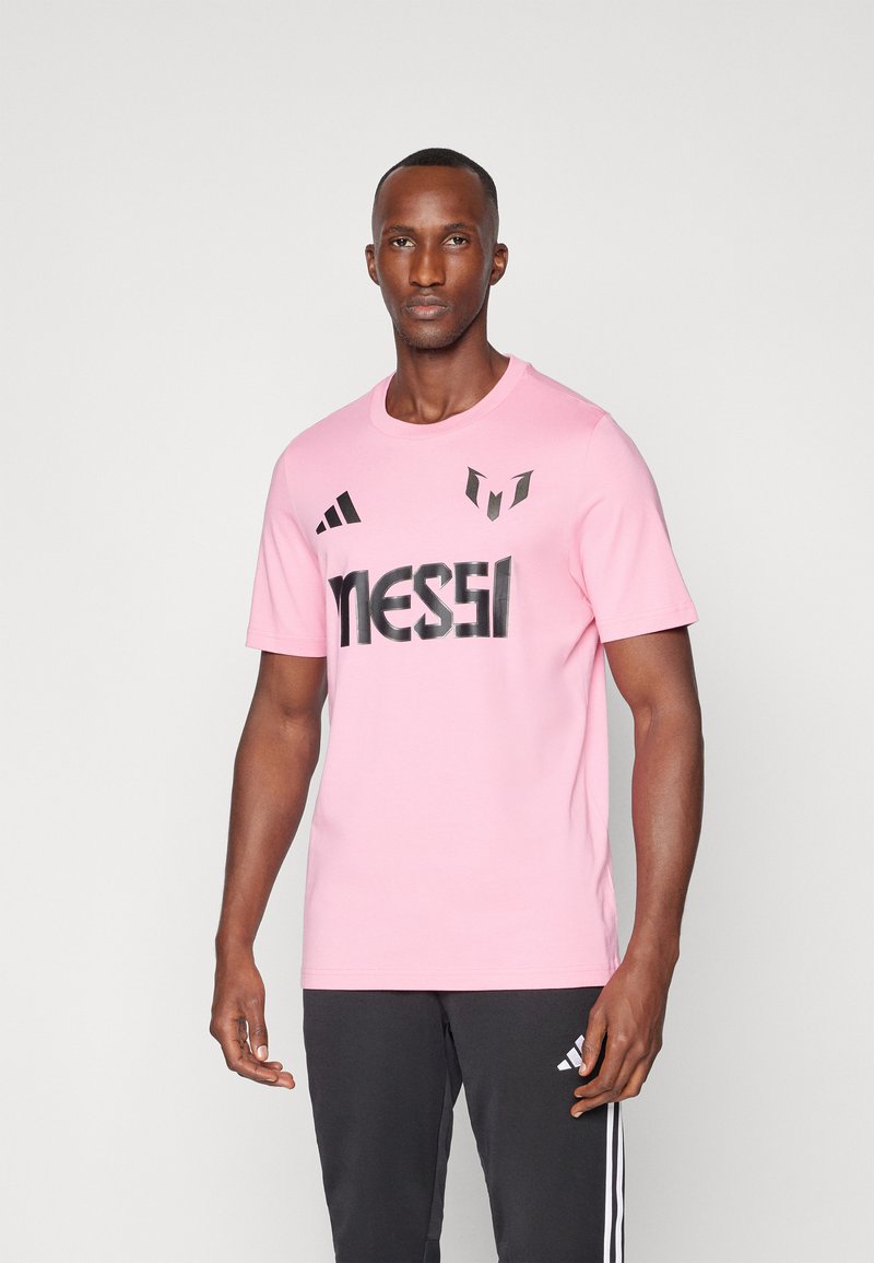 Pink t-shirt made of cotton with short sleeves, featuring black "MESSI" logo and accents from Adidas. Simple round neckline and casual fit.