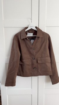Veste en daim marron avec un col, deux poches avant et une fermeture à boutons. Texture lisse avec un design classique.