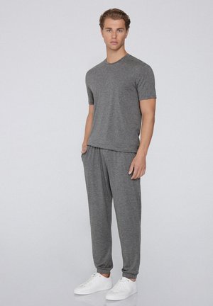 Completo sportivo grigio composto da una maglietta a maniche corte e pantaloni jogger coordinati, realizzati in un tessuto morbido e testurizzato. Inclusi sneakers bianche.