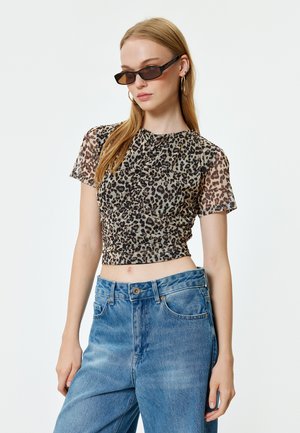 Luipaardprint, semi-doorzichtig, korte mouwen crop top met gerimpelde details. Gecombineerd met hooggetailleerde, lichtblauwe denim jeans.