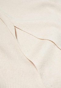 Crème-kleurige gebreide stof met een geribbeld patroon, featuring overlappende lagen en een gladde afwerking. Subtiele variaties in de weving zijn zichtbaar.