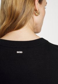 Vêtement en tricot noir avec un col plat et un petit logo "BOSS" brodé à l'arrière du col. Texture lisse et coupe ajustée.