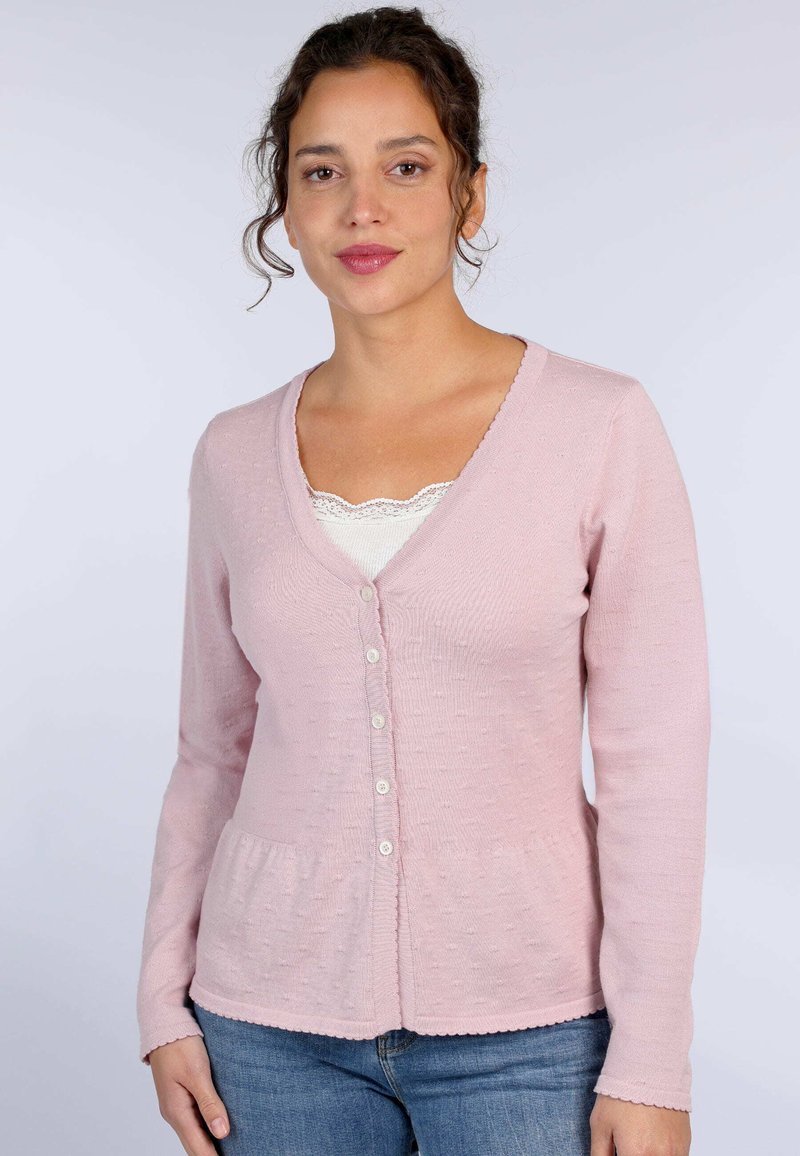 Rosa Strickjacke mit V-Ausschnitt, strukturiertem Stoff, Knopfverschluss und gewelltem Saum. Kombiniert mit einem weißen Spitze-Camisole darunter.