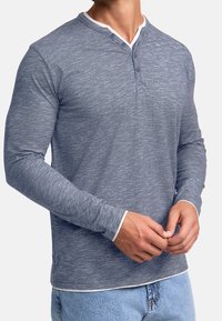 Long-sleeve henley shirt in melange blue fabric. Features a white collar trim, three-button placket, and a fitted silhouette.