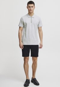 Kortærmet grå polo shirt med lynlås krave, parret med sorte shorts og sorte loafers. Stoffet ser glat og let ud.
