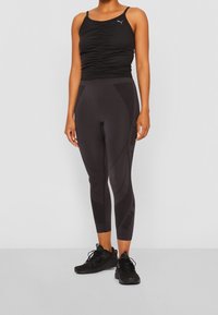 Czarny sportowy top na ramiączkach z drapowaniem, zestawiony z czarnymi legginsami z teksturowanym wzorem i logo. Oba wykonane z elastycznego materiału.