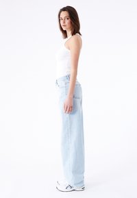 Vaaleansiniset ylisuuret farkut, joissa on korkeavyötäröinen ja suora lahje, yhdistettynä valkoiseen slim fit -toppiin ja tennareihin.