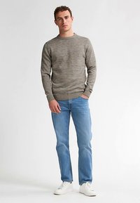 Grauer, strukturierter Pullover mit rundem Ausschnitt und gerippten Bündchen, getragen zu hellblauen Jeans und weißen Sneakers, vor neutralem Hintergrund stehend.