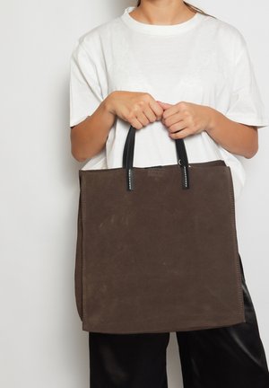 Braune Wildleder-Umhängetasche mit schwarzen Ledergriffen, rechteckige Form, glatte Textur und dezente Stichdetails an den Nähten.