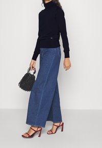 Laivastonsininen pooloneuletakki, leveälahkeiset siniset farkut, viininpunaiset korkokengät ja musta punottu käsilaukku.