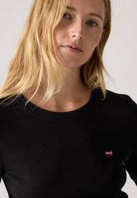 Černé bavlněné tričko s dlouhým rukávem a kulatým výstřihem. Má malý červený logo Levi's na levé horní části hrudi. Hladká textura.