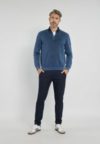 Granatowy longsleeve pulower z kołnierzykiem, o fakturowanym wykończeniu. Zestawiony z ciemnymi spodniami w prążki i białymi trampkami.