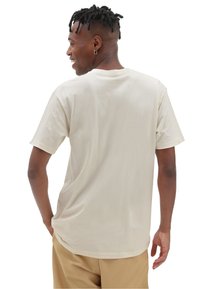 Camiseta beige de mangas cortas, hecha de una tela suave, con un escote redondo y un corte relajado. Textura lisa sin patrones ni acentos visibles.