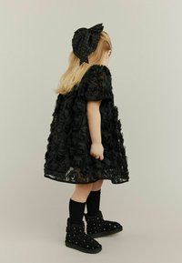 Crna haljina s trodimenzionalnim detaljima ruža, uparena s velikom crnom mašnom s točkicama za kosu, crnim čarapama i ukrašenim crnim čizmama.