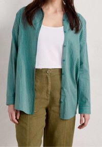Turquoise gestreept shirt met lange mouwen, knoopsluiting en een relaxte pasvorm, gedragen over een witte tanktop en olijfgroene broek.