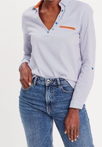 Collared, button-up shirt featuring a blue and white pattern, a brown accent on the collar, and a chest pocket. Worn with blue jeans.