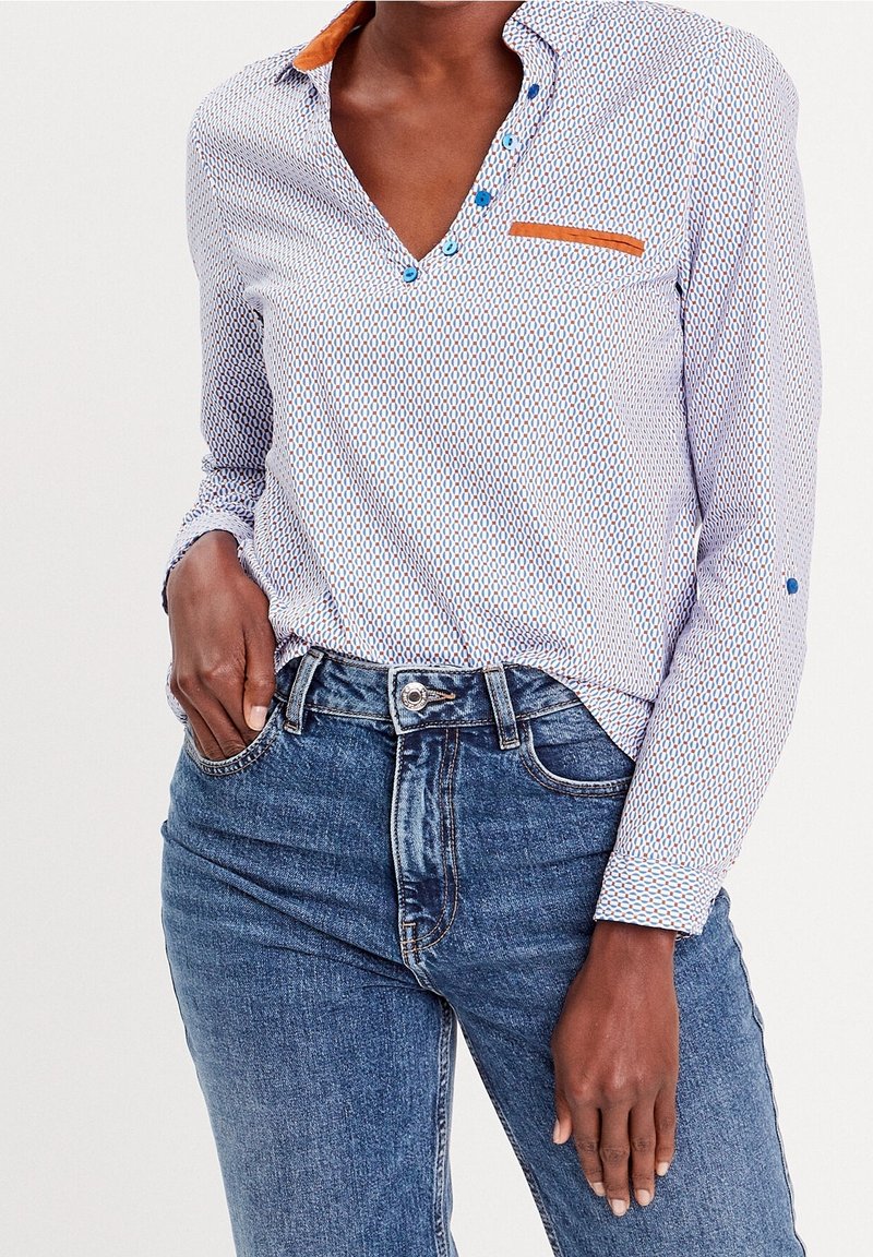 Collared, button-up shirt featuring a blue and white pattern, a brown accent on the collar, and a chest pocket. Worn with blue jeans.