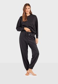 Sudadera negra con cuello redondo, corte holgado y mangas largas; combinada con pantalones jogger a juego que tienen una cintura elástica y puños.