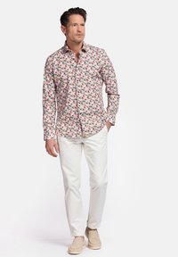 Chemise blanche à boutons avec un motif floral coloré, associée à un pantalon de couleur claire et des chaussures beiges. Le design présente un col évasé et des manches longues.