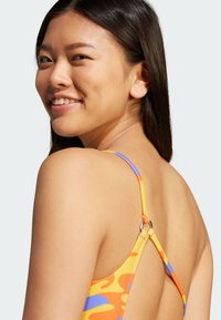 Χρωματιστό, μοτίβο μαγιό με κίτρινη βάση και πορτοκαλί και μπλε λεπτομέρειες, ρυθμιζόμενους ιμάντες και κυκλικό μεταλλικό στοιχείο.