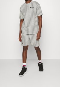 Grårandig kortärmad skjorta och matchande shorts, med svarta horisontella ränder och logobroderi, som bärs med svarta sneakers och vita strumpor.