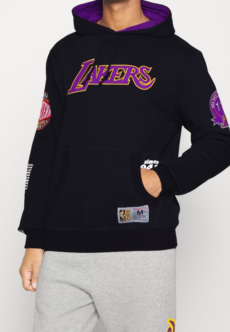 Felpa nera con fodera viola, caratterizzata da logo ricamato dei "Lakers", toppe sulle maniche, tasca a marsupio e etichetta hardware NBA sull'orlo.