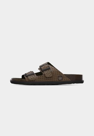 Brun slip-på sandal med to justerbare spænderemme og tekstureret stjernekontrast på overdelen, flad sort sål og cirkulært logo på siden.