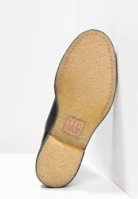 Suola di scarpa in pelle nera con una base in gomma leggera marrone chiaro, caratterizzata da una finitura texturizzata, un bordo cucito e un'etichetta con il logo.