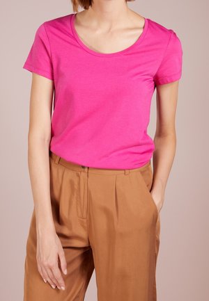 Camiseta de manga corta y cuello redondo en rosa vibrante, confeccionada en tela suave. Combinada con pantalones plisados de color marrón claro, con un ajuste relajado.