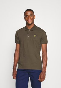 Mørkegrønn polo-skjorte med korte ermer, tre-knapps placket, og en gul logo på venstre bryst. Glatt tekstur og tilpasset design.