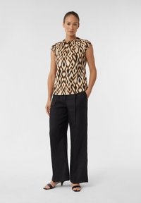 Ärmelloses Oberteil mit abstraktem braun-beigen Muster; schwarze weit geschnittene Hose; weicher Stoff mit leichtem Glanz; minimalistisches Design; flache schwarze Sandalen.