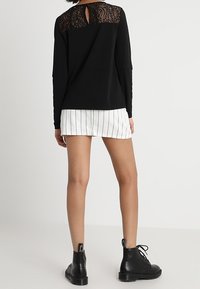 Svart långärmad topp med spetsdetaljer på ryggen, parat med vita randiga shorts och svarta snörade ankelkängor.