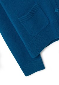 Cárdigan de punto en color verde azulado con un acabado texturizado, que presenta un único bolsillo en la parte delantera y puños acanalados. Los botones son redondos y del mismo color.