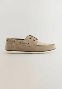 Pantofii de barcă din suede bej, cu bară superioară perforată, două găuri pentru șireturi, talpă albă contrastantă și o textură netedă.
