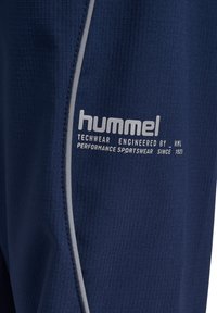 Navy techwear shorts med texturerad tyg, slim fit, reflekterande grå kant och Hummel-logotyp i vitt. Hållbar konstruktion som är idealisk för prestanda.