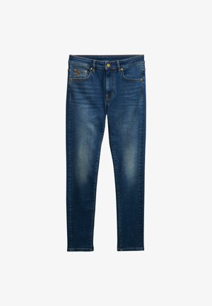 Jeans de mezclilla azul oscuro con un diseño de pierna recta, parches deslavados y herrajes de cobre, incluyendo un botón y remaches. Estilo clásico de cinco bolsillos.