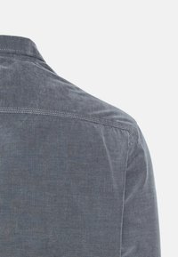 Dunkelblaues, strukturiertes Hemdenmaterial mit einem dezenten Muster. Verfügt über einen Kragen und Details an der Schulternaht. Rückansicht, die keine zusätzlichen Designelemente zeigt.
