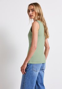 Ärmlös, ljusgrön linne med en figurnära design. Mjuk textur, rund halsringning och avslappnad passform i kombination med högmidjade blå jeans.