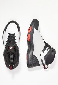Valkoiset ja mustat vaelluskengät punaisilla yksityiskohdilla, joissa on teksturoitu pinta, nauha suljenta ja kestävä kumipohja pidon takaamiseksi.