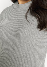 Pull en maille côtelée gris, à col roulé, présentant un design ajusté avec des rayures verticales et une encolure haute, fabriqué en tissu doux.