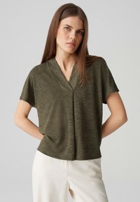 Top corto a maniche corte verde oliva con scollatura a V e vestibilità comoda, caratterizzato da un tessuto testurizzato e un sottile motivo mélange.
